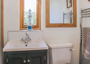 Ein Badezimmer mit einem weißen Waschbecken, einer Toilette, einem Fenster mit Blick auf Grünflächen und einem Spiegel über dem Waschbecken.