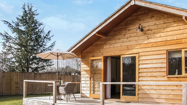 Une cabane en bois avec une terrasse, une table et des chaises, et un grand parasol.