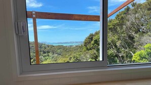 Ein Zimmer mit großem Fenster, das auf eine bewaldete Gegend und eine ferne Küstenlinie blickt.