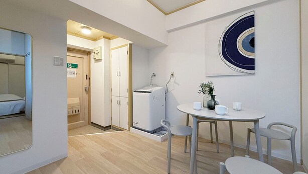 A hotel room with a bed, a small table with chairs, a wall-mounted artwork, and a kitchenette.