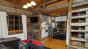 A rustic cabin interior with a dining area, kitchen, and a television.