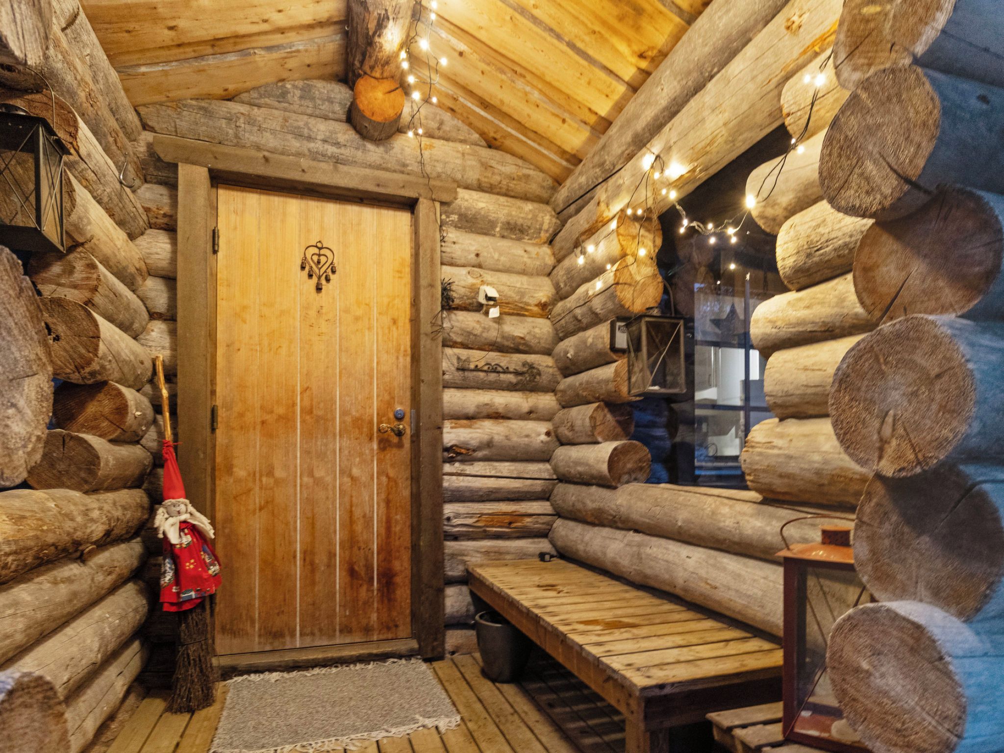 A log cabin interior with a wooden door, a bench, and string lights.