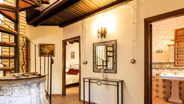 A room with a large rustic barrel, a bed with a red blanket, a mirror above a console table, and a bathroom with patterned tiles. - Complex of 2 houses with swimming pool, (Melegís)