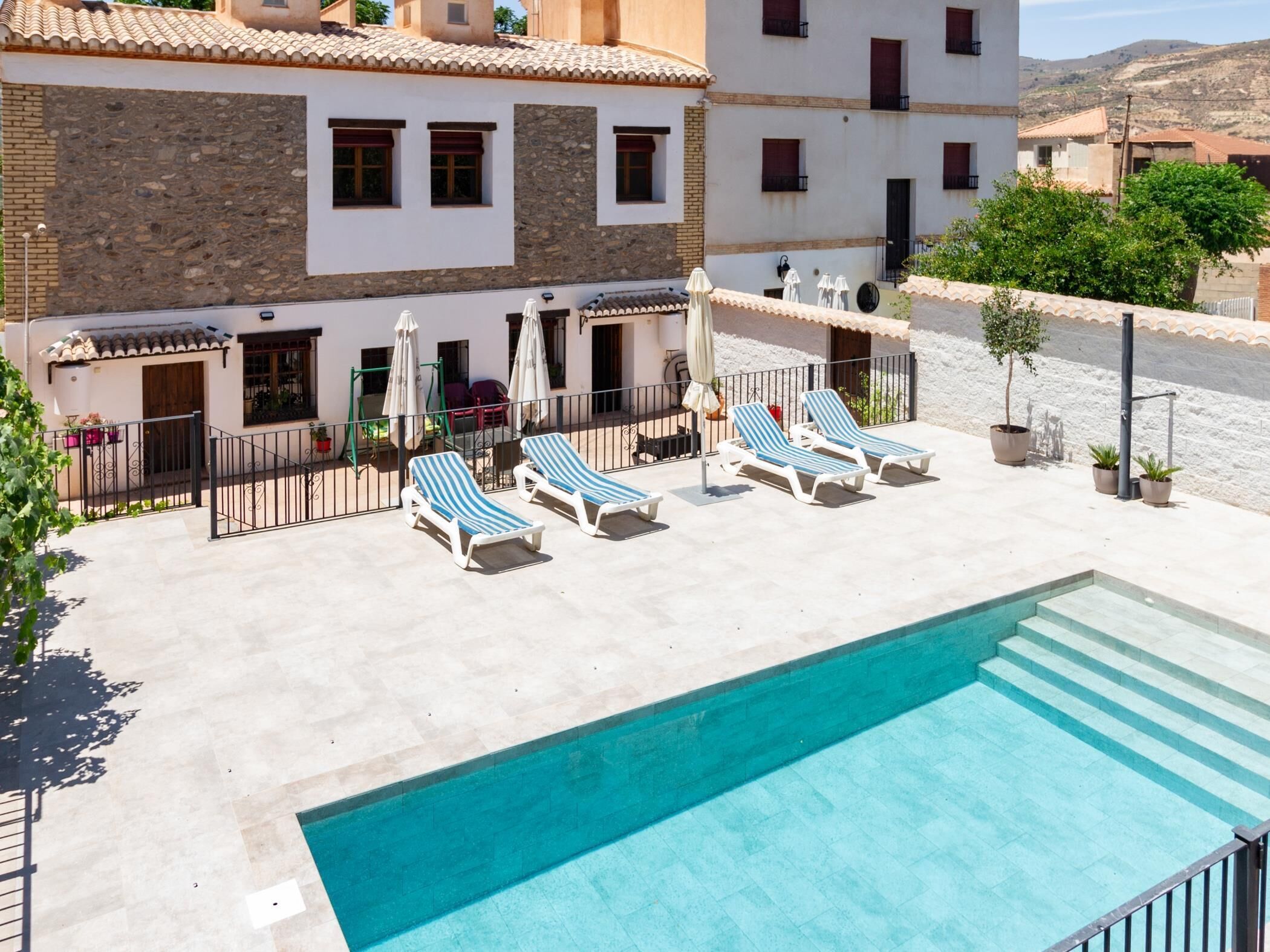 A pool area with lounge chairs and a building with a tiled roof and stone facade.