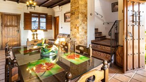 A dining area with a glass table, wooden chairs, a stone wall, and a staircase. - Complex of 2 houses with swimming pool, (Melegís)