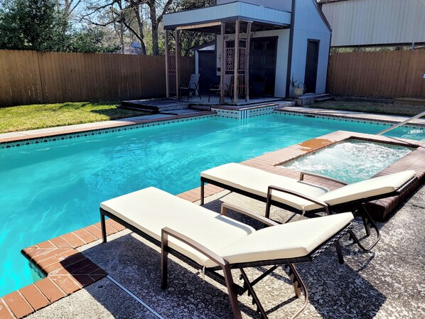 A backyard with a swimming pool, lounge chairs, and a covered patio area.