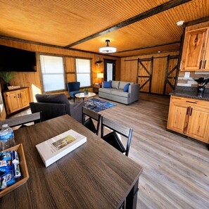 A spacious living area with a wooden ceiling, a sofa, a coffee table, and a dining table with chairs. - BASShole on Lake Fork - Waterview - Boat Ramp - Hot Tub (Quitman)