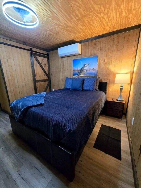 A bedroom with a bed, a nightstand, a lamp, a painting, and a ceiling light fixture.