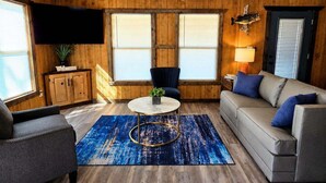 Un salón con suelo de madera, un sofá, un sillón y una mesa de centro redonda.