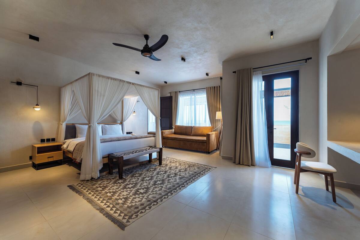 A spacious bedroom with a large bed, a ceiling fan, a sofa, and a chair.