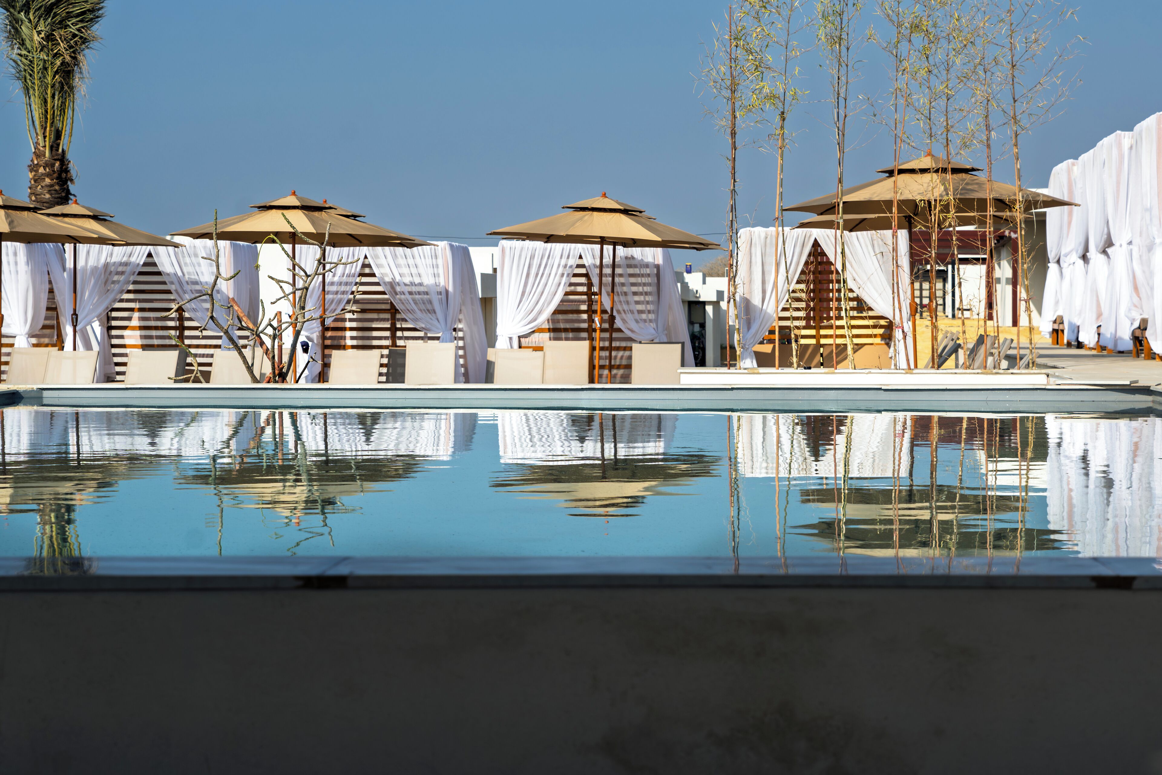 Zona junto a la piscina con sombrillas y zonas de estar cubiertas, reflejado en el agua.