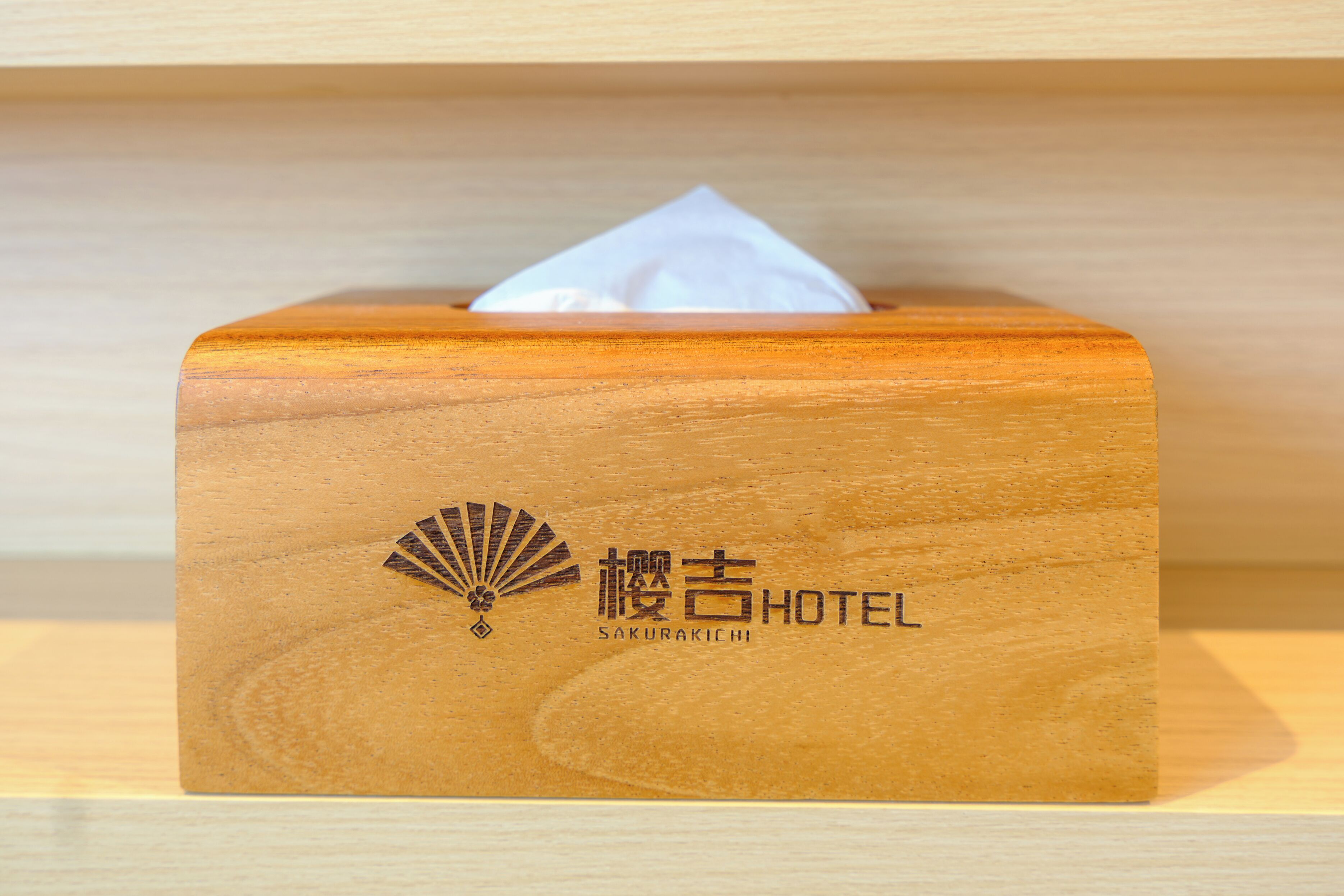 A wooden tissue box with a fan and hotel name on it.