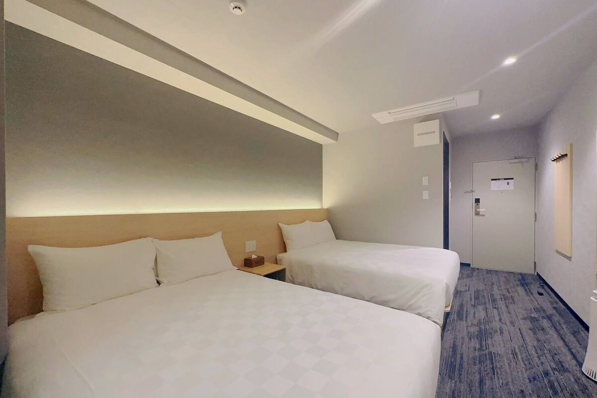 A hotel room with two beds, a wooden headboard, a nightstand, and a door with a sign.