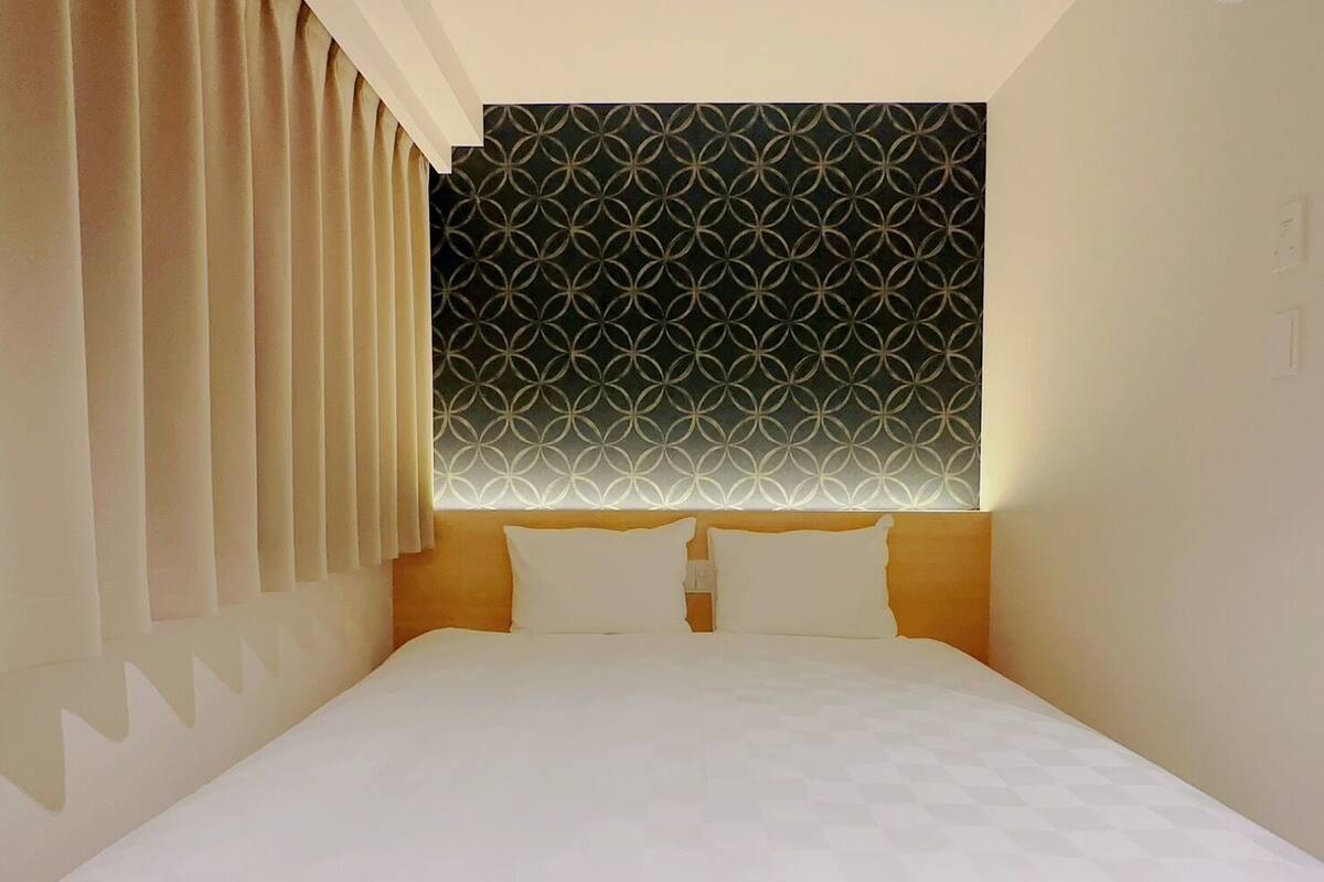 A hotel room with a bed, curtains, and a patterned wall.
