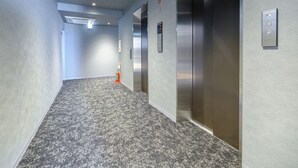 A hallway with a carpeted floor, two elevators, and a fire extinguisher. - SAKURAKICHI HOTEL (Izumisano)