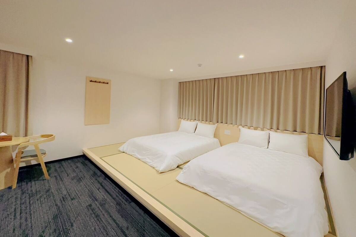 A hotel room with two single beds, a desk, and a television.