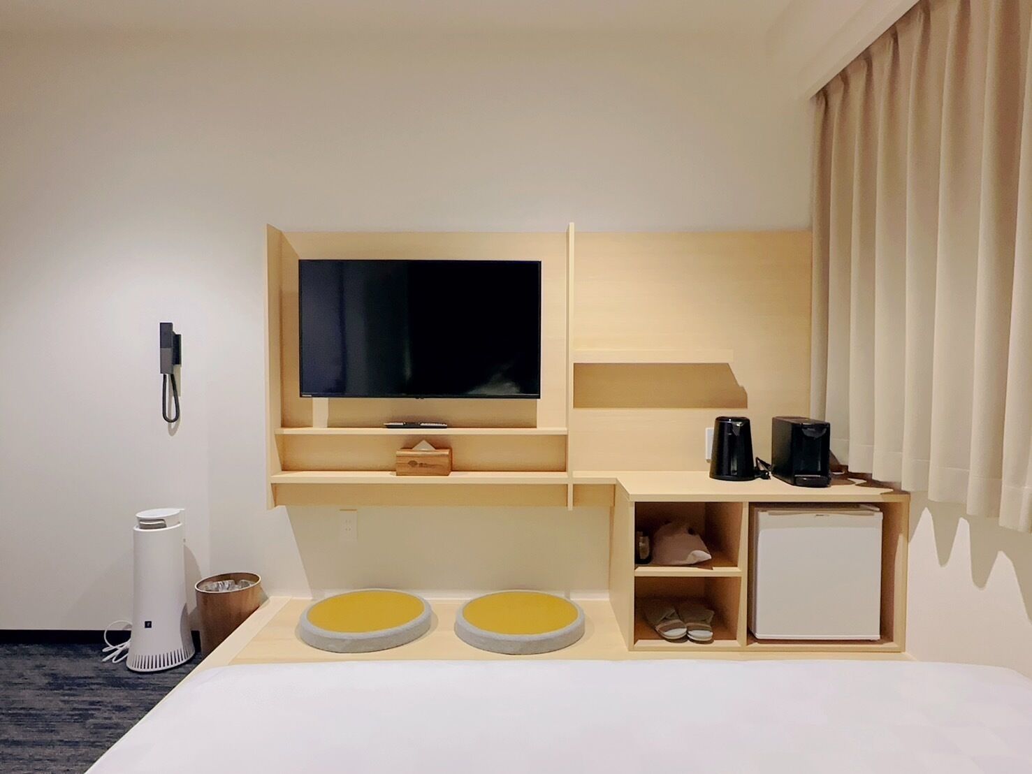 A hotel room with a bed, a TV mounted on the wall, a coffee maker, and a small cabinet.