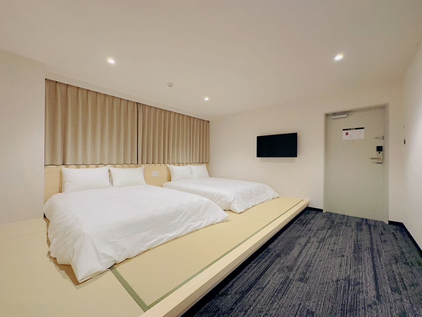 Een hotelkamer met twee bedden, een wandtelevisie en een deur met een bordje.