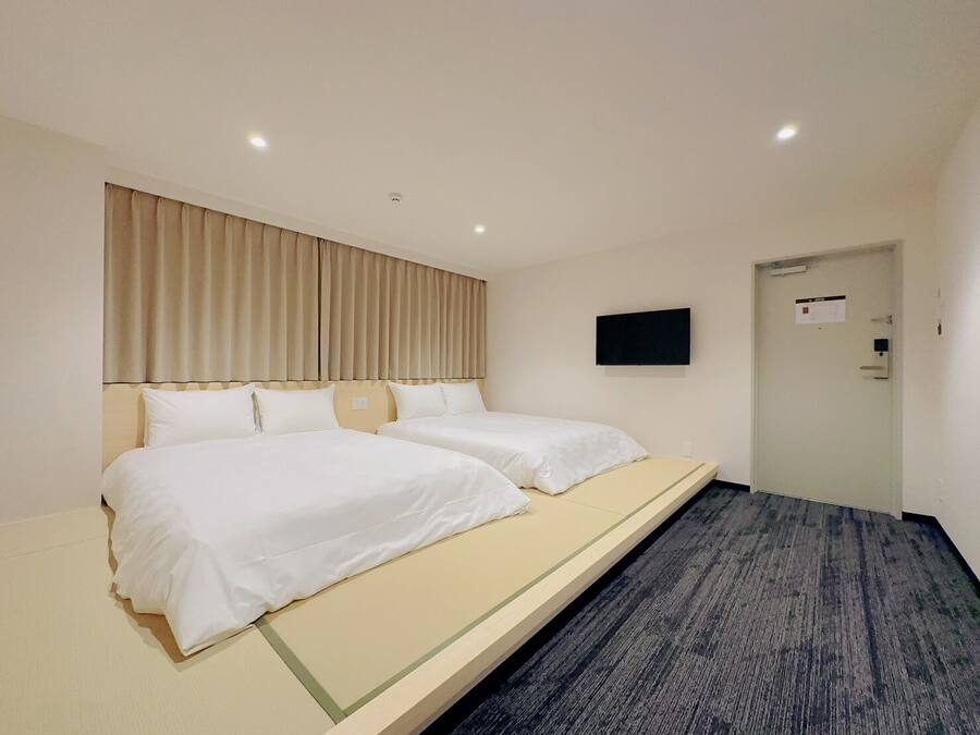 A hotel room with two beds, a flat-screen TV mounted on the wall, and a door with a sign.