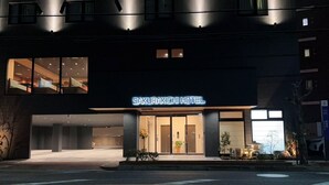 The exterior of the Sakurakichi Hotel with a modern facade, large windows, and a well-lit entrance. - SAKURAKICHI HOTEL (Izumisano)