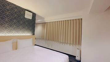 A hotel room with a large bed, a patterned wall, a window with curtains, and a ceiling light.