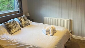 A neatly made bed with white linens and two patterned pillows, a white radiator, and a window with curtains.