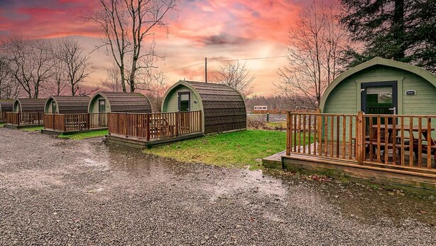 A row of small, green-roofed cabins with wooden railings, set against a backdrop of trees and a dramatic sky.