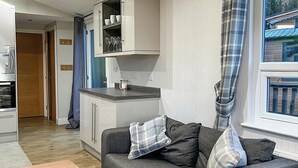 A modern living room with a grey sofa, a wooden coffee table, and a kitchen area with white cabinets and a built-in oven.