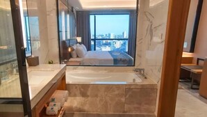 A modern hotel room with a large bed, a glass-enclosed bathroom, and a city view. - Rising Dragon International Hotel (Dongguan)