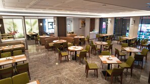 A modern restaurant with round tables and green chairs, marble flooring, and large windows.