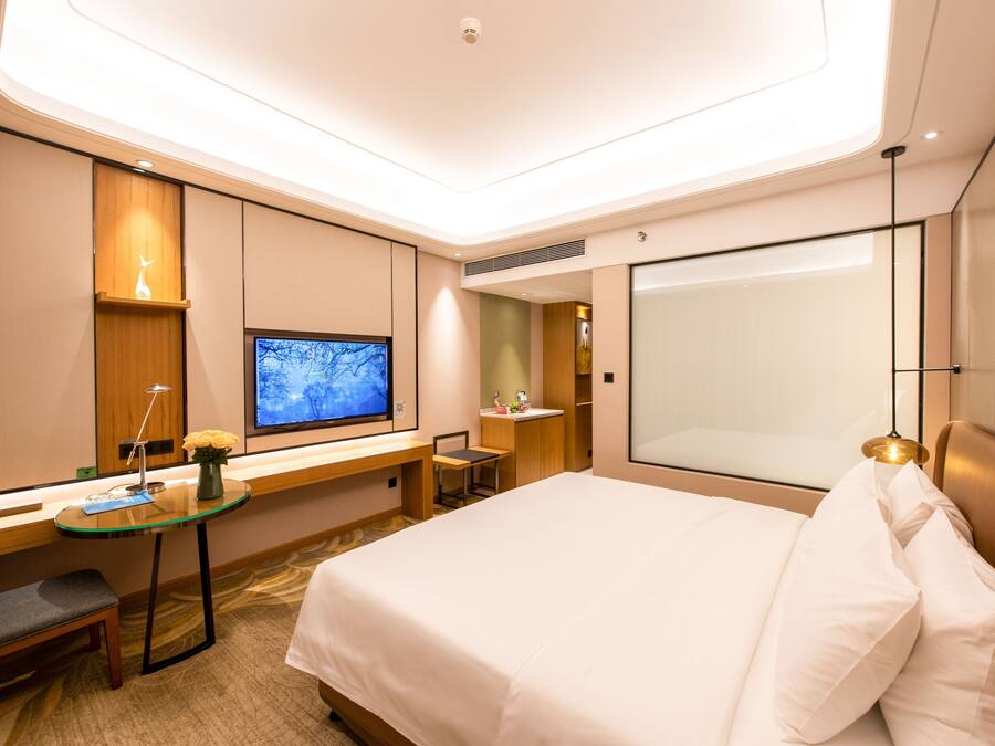 A modern hotel room with a large bed, a desk with a computer, a television, and a large window.