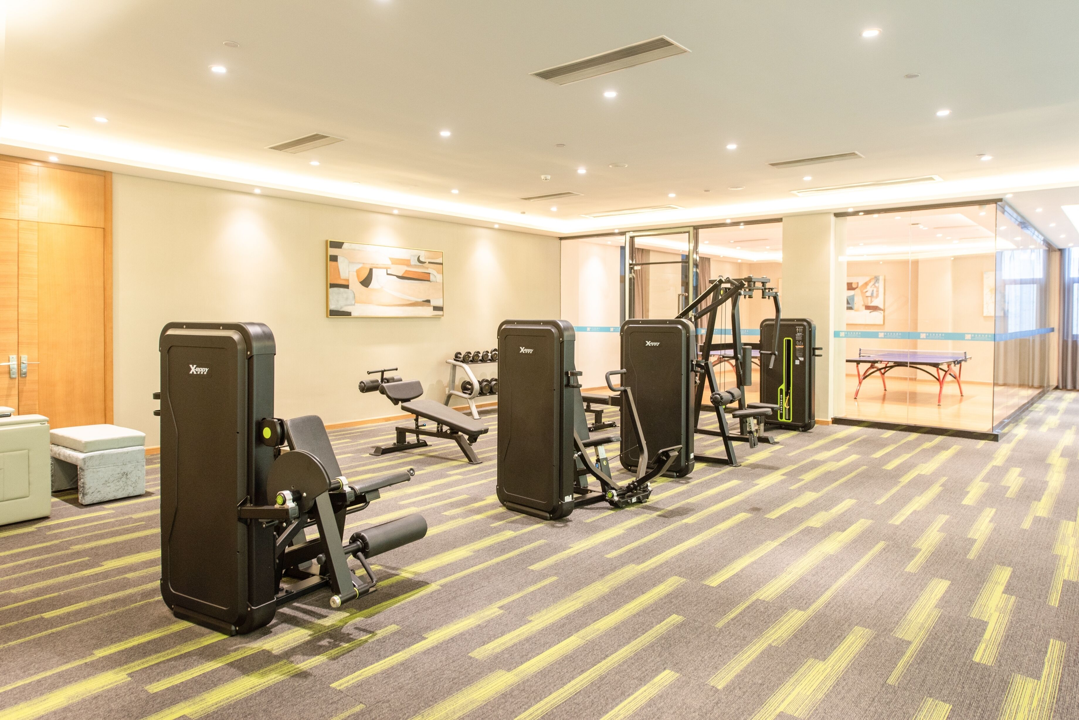 A gym with various exercise machines, a bench, and a wall-mounted artwork.