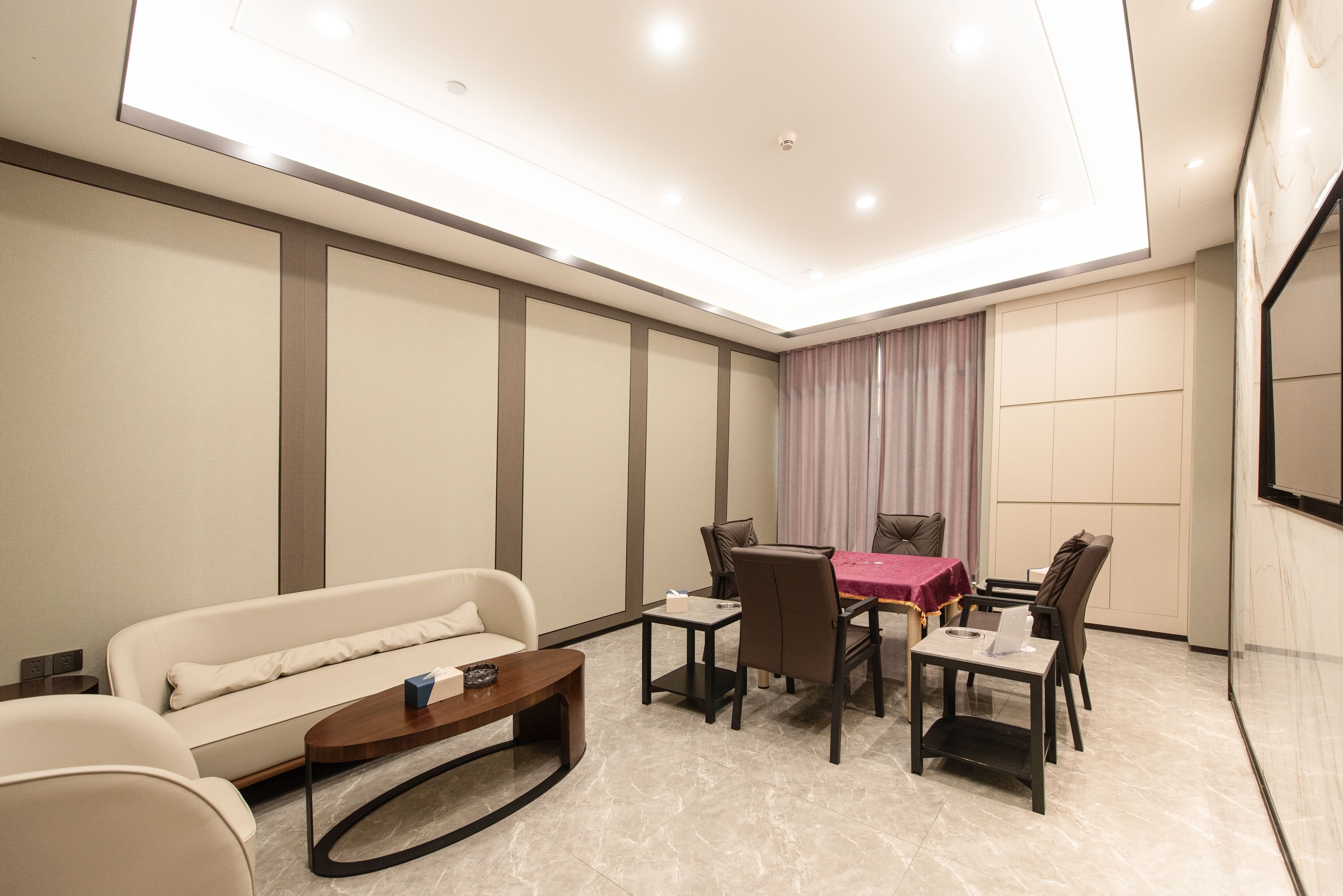 A modern hotel room with a sofa, dining table, chairs, and a TV.