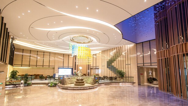 A spacious lobby with a central fountain, a staircase, and a large digital screen displaying a blue sky. - Rising Dragon International Hotel (Dongguan)