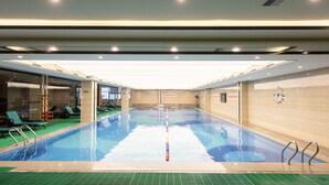 An indoor swimming pool with clear water, surrounded by lounge chairs and a tiled wall. - Rising Dragon International Hotel (Dongguan)