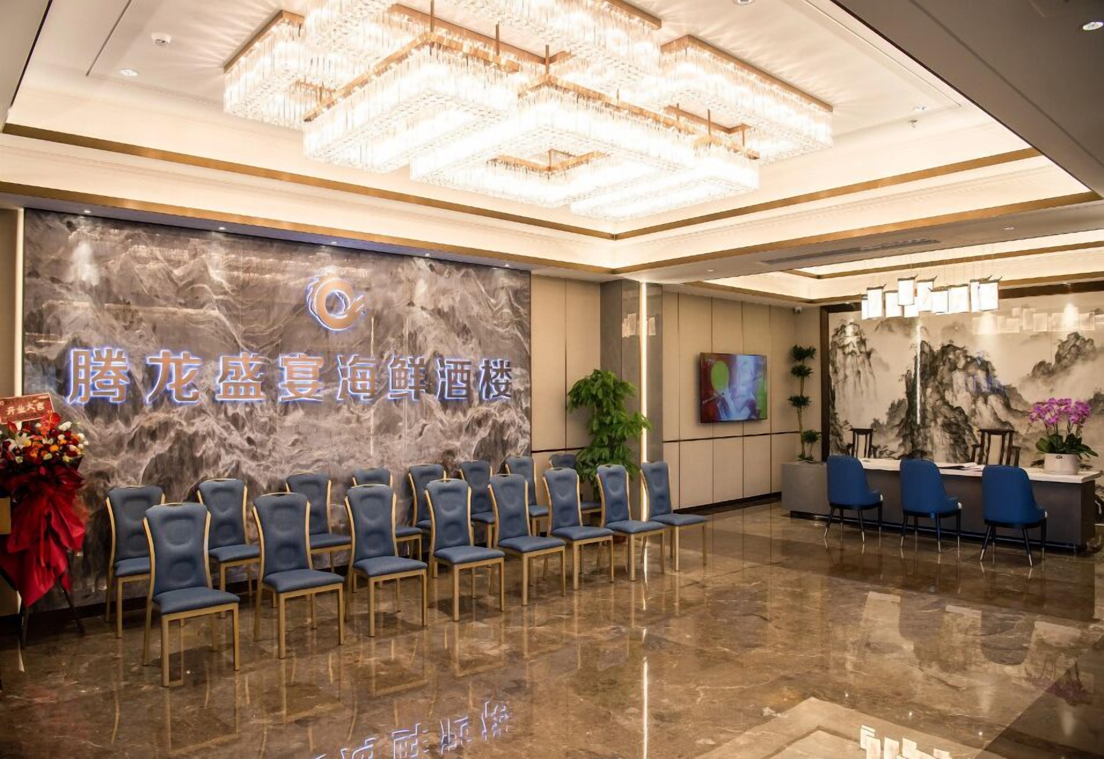 A hotel lobby with a marble reception desk, blue chairs, and a chandelier.