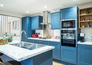 A modern kitchen with blue cabinets, a stainless steel range hood, a built-in oven, and a coffee maker.