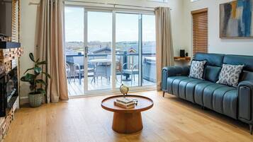 Un salon spacieux doté d’une grande porte-fenêtre coulissante donnant sur un balcon, d’un canapé en cuir et d’une table basse en bois.