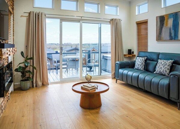 A spacious living room with a large sliding glass door leading to a balcony, a leather sofa, and a wooden coffee table.