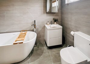 A modern bathroom with a freestanding bathtub, a sink with a mirror, and a toilet.