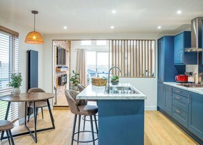 A modern kitchen with a central island, a dining area with a round table and chairs, and a view through a large window.