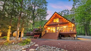 A cabin with a wooden exterior, a porch, and a stone chimney. - Lakehouse w/ Kayaks, MiniGolf, Sauna, HotTub, Swings and playground for Kids! (Pocono Summit)