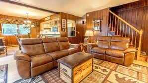 A cozy living room with leather sofas, a wooden chest, and a staircase. - Lakehouse w/ Kayaks, MiniGolf, Sauna, HotTub, Swings and playground for Kids! (Pocono Summit)