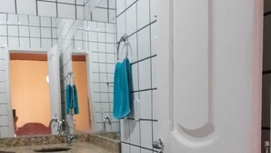 A bathroom with white tiled walls, a sink with a beige countertop, and a mirror. There are two towels hanging on hooks.