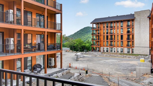 A multi-story building with balconies, a parking area, and a mountainous backdrop.