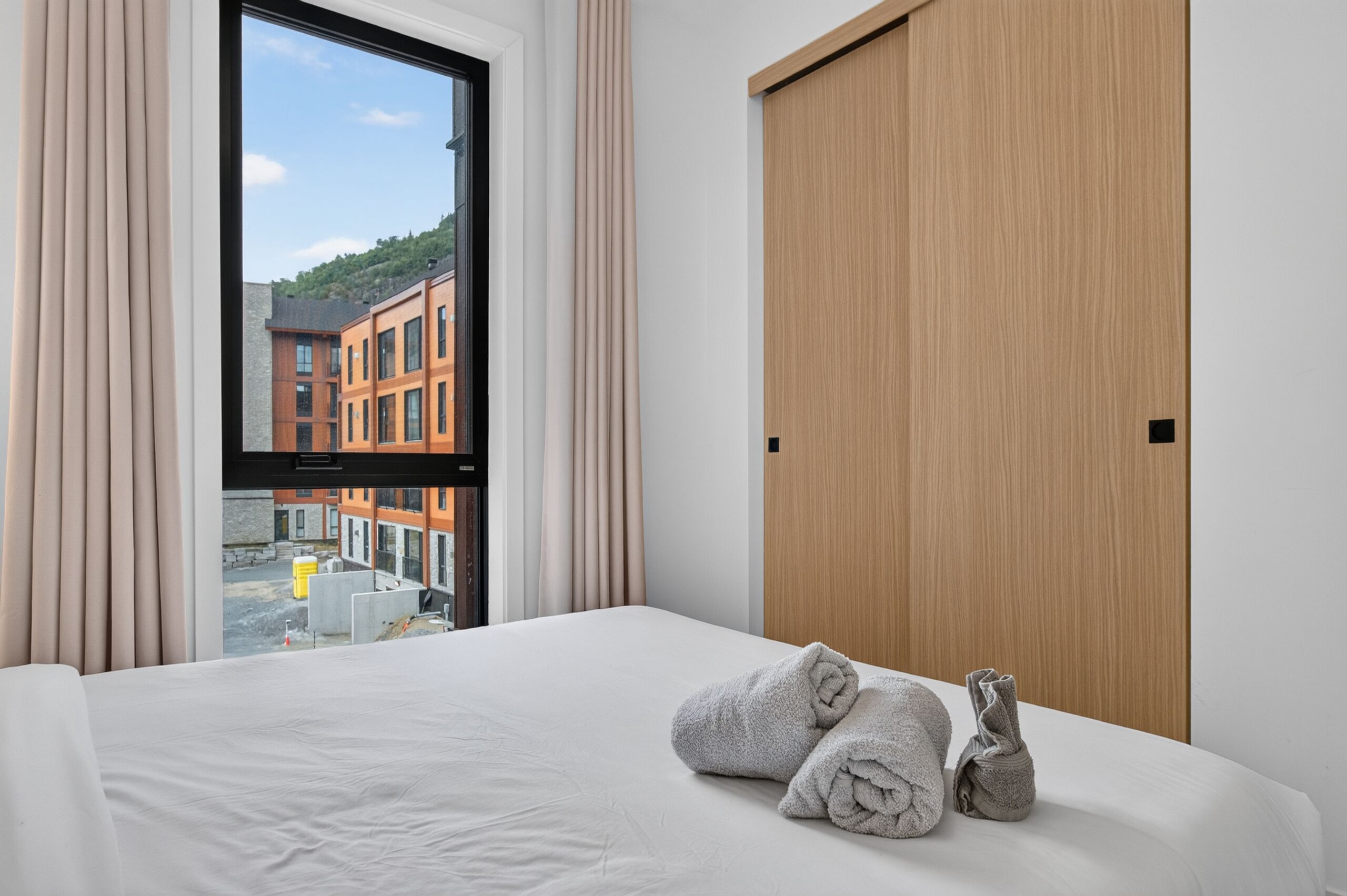 Habitación de hotel con cama, ventana con cortinas, vista a un edificio y puerta de madera.
