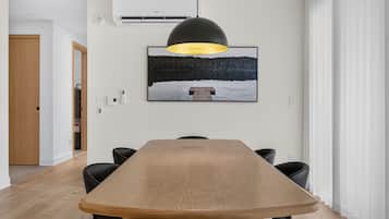 Uma área de refeições com uma mesa de madeira comprida, cadeiras pretas, uma luminária pendente e um quadro na parede.