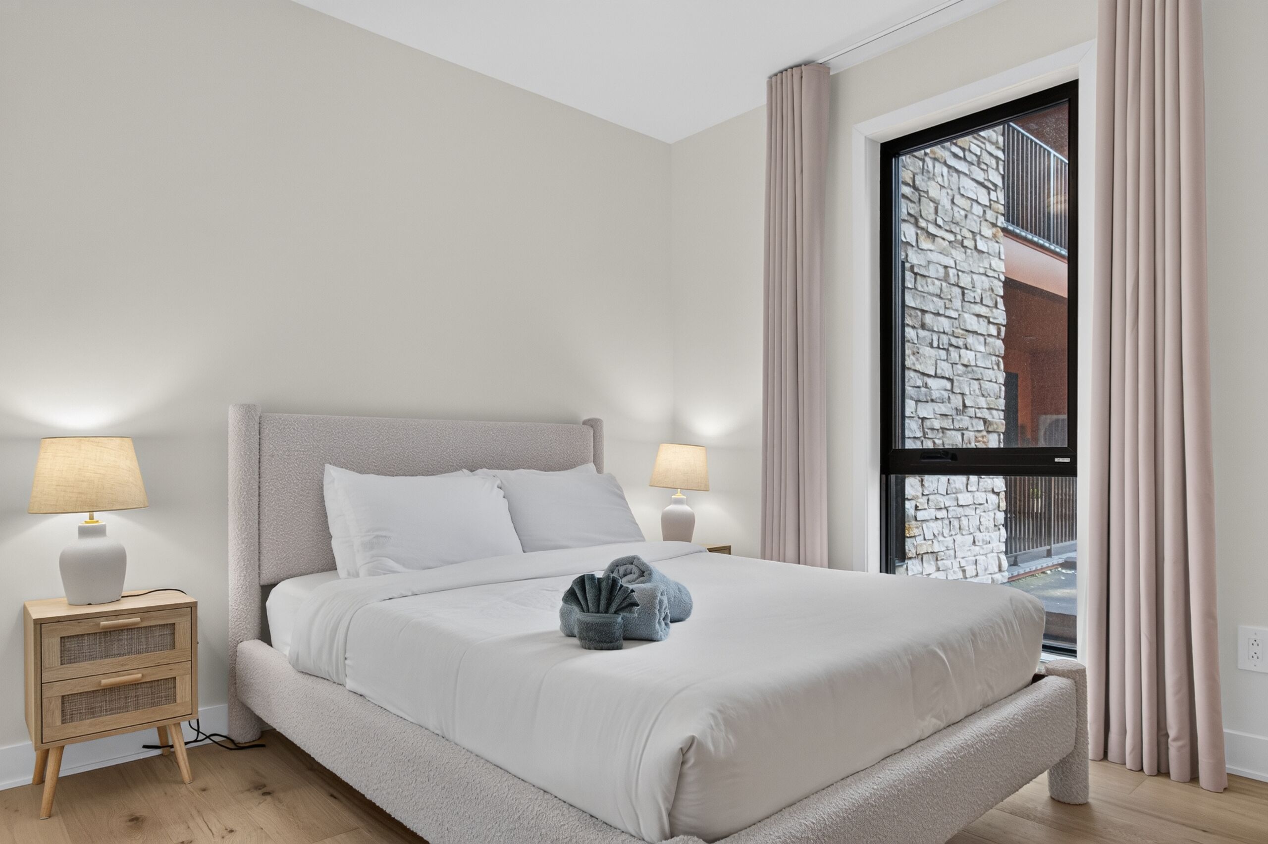 Una camera da letto ordinata con un letto, lampade da comodino, un comodino e una finestra con tende.
