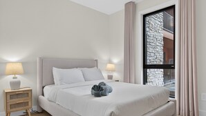 A neatly arranged bedroom with a bed, bedside lamps, a nightstand, and a window with curtains.