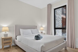 Une chambre à coucher bien rangée, avec un lit, des lampes de chevet, une table de nuit et une fenêtre avec des rideaux.